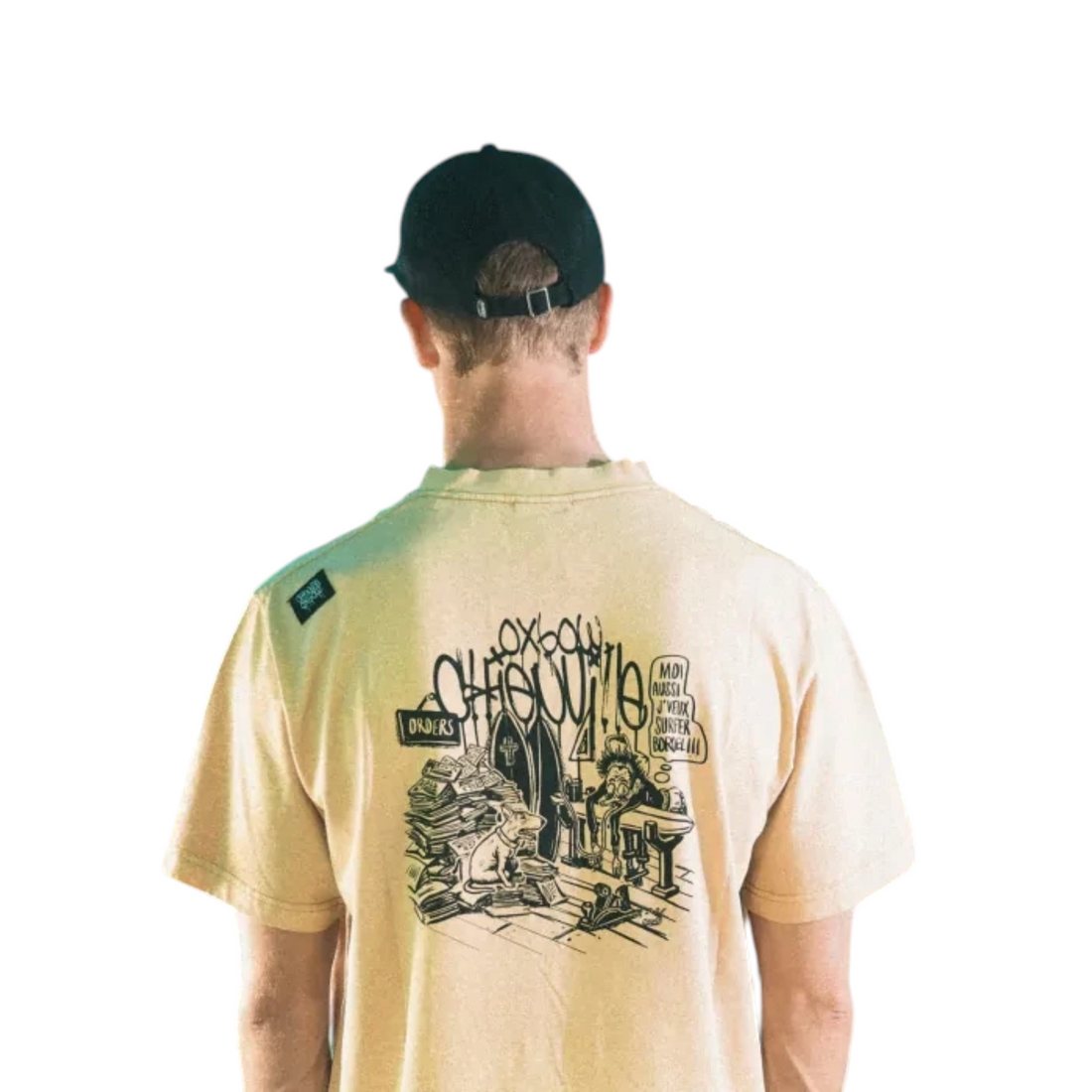 Homme portant une casquette noire Born2ride et un t-shirt beige avec illustration surf devant des planches de surf