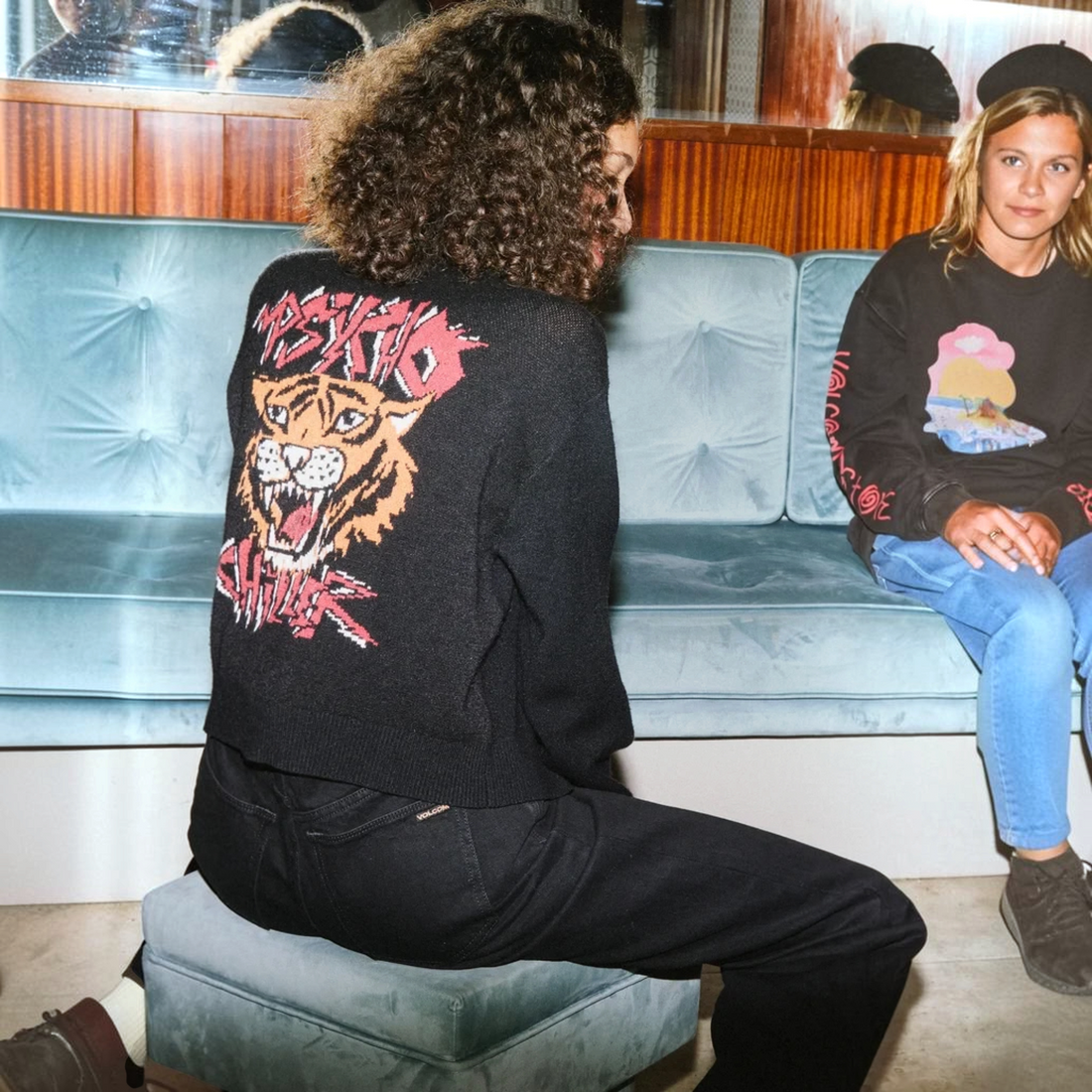 Cardigan noir Born2ride Volcom Fa Ozzy avec motif tigre vintage au dos porté par une femme sur un canapé en velours