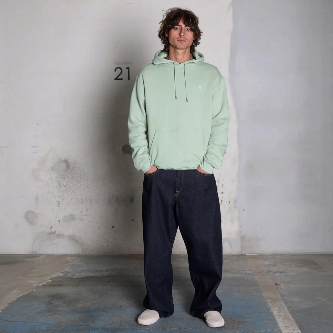 Homme portant un jean Born2ride Volcom Billow Denim brut et un sweat à capuche vert menthe dans un décor industriel