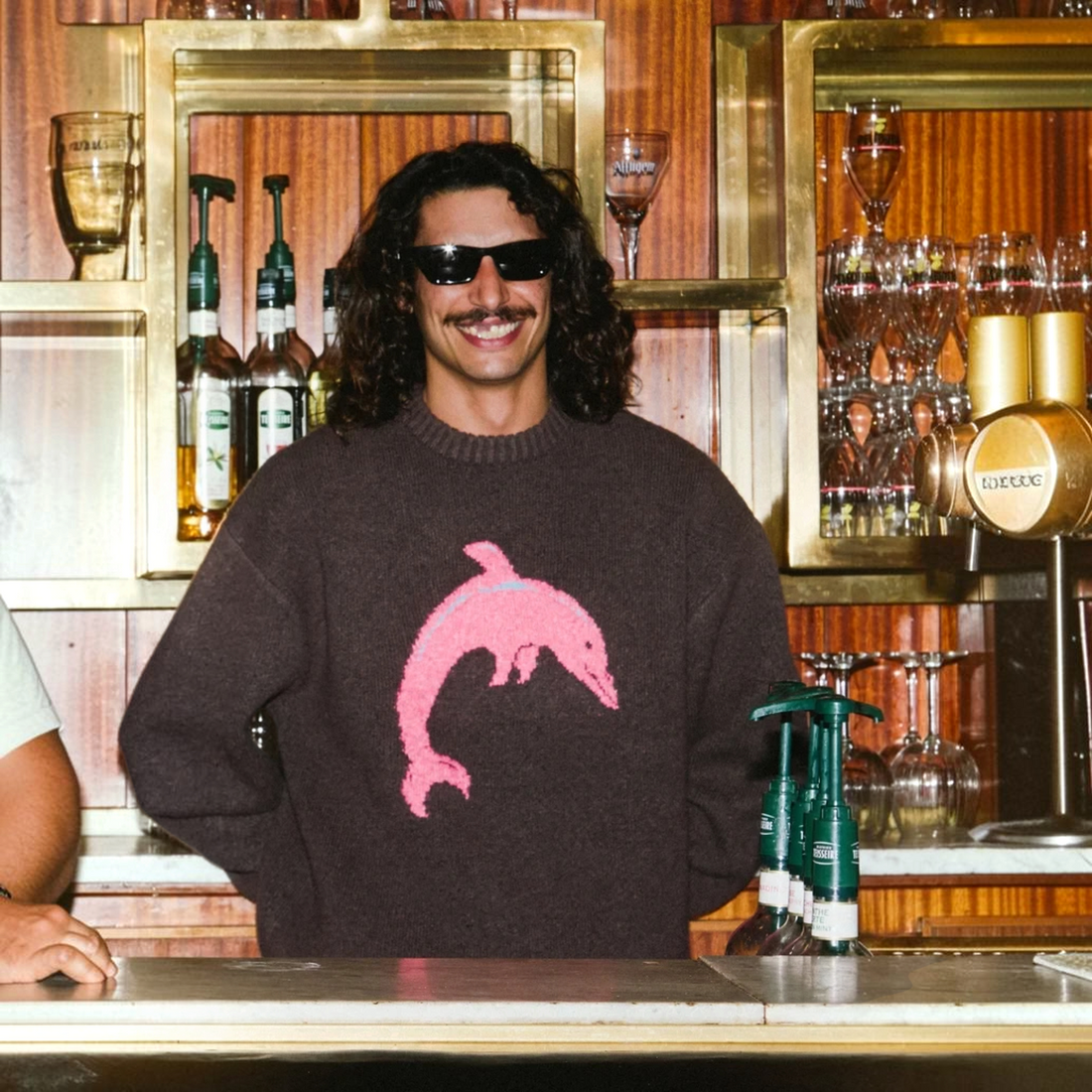 Homme portant le pull Born2ride Volcom Fa Ozzy Dolphin couleur raisin avec un motif dauphin rose au bar